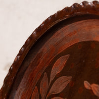 Close-up detail of a dark brown wooden decorative tray with a scalloped edge and leaf inlay pattern.