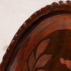 Close-up detail of a dark brown wooden decorative tray with a scalloped edge and leaf inlay pattern.