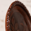 Close-up of a dark brown carved wooden tray or plate with a scalloped rim and leaf-like relief details, photographed against a softly blurred light background.