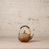Brown ceramic teapot with a textured surface and wicker handle on a light gray background