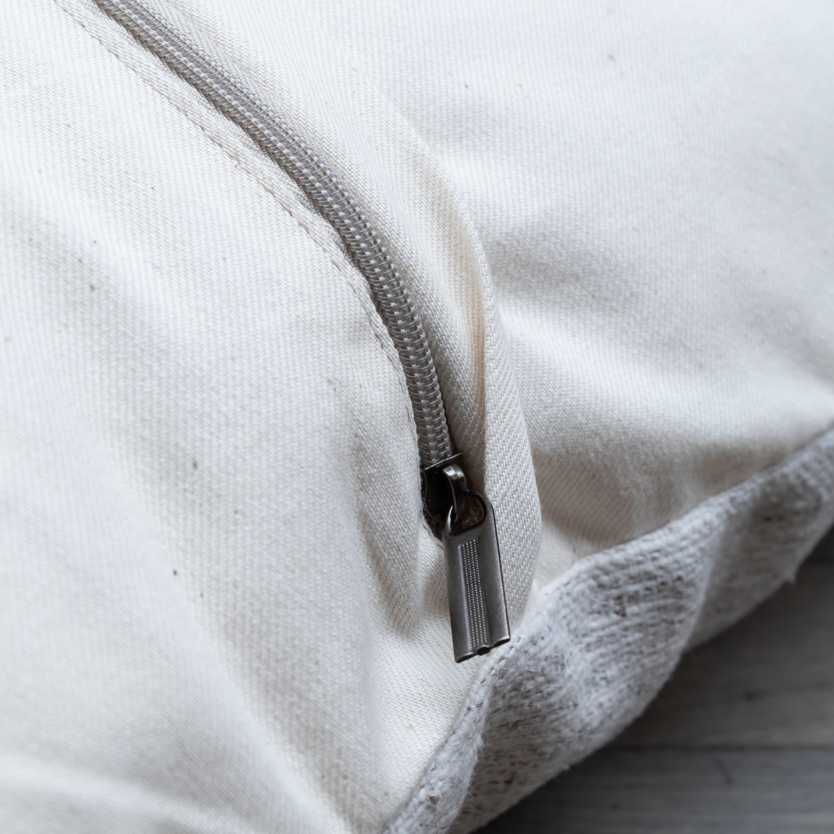 Close-up of a cream canvas zipperpered pouch or bag with a silver metal zipper pull, showing the texture of the fabric and the edge of the zipper tape.