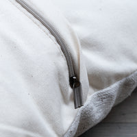 Close-up of a cream canvas zipperpered pouch or bag with a silver metal zipper pull, showing the texture of the fabric and the edge of the zipper tape.