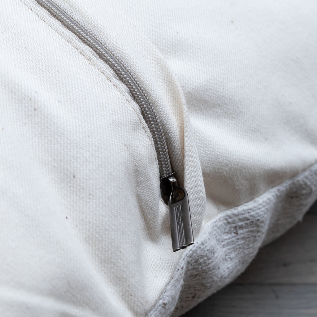 Close-up of a cream canvas zipperpered pouch or bag with a silver metal zipper pull, showing the texture of the fabric and the edge of the zipper tape.