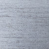 A close-up of a woven fabric texture in a light blue-gray color with subtle darker gray and brown flecks throughout.