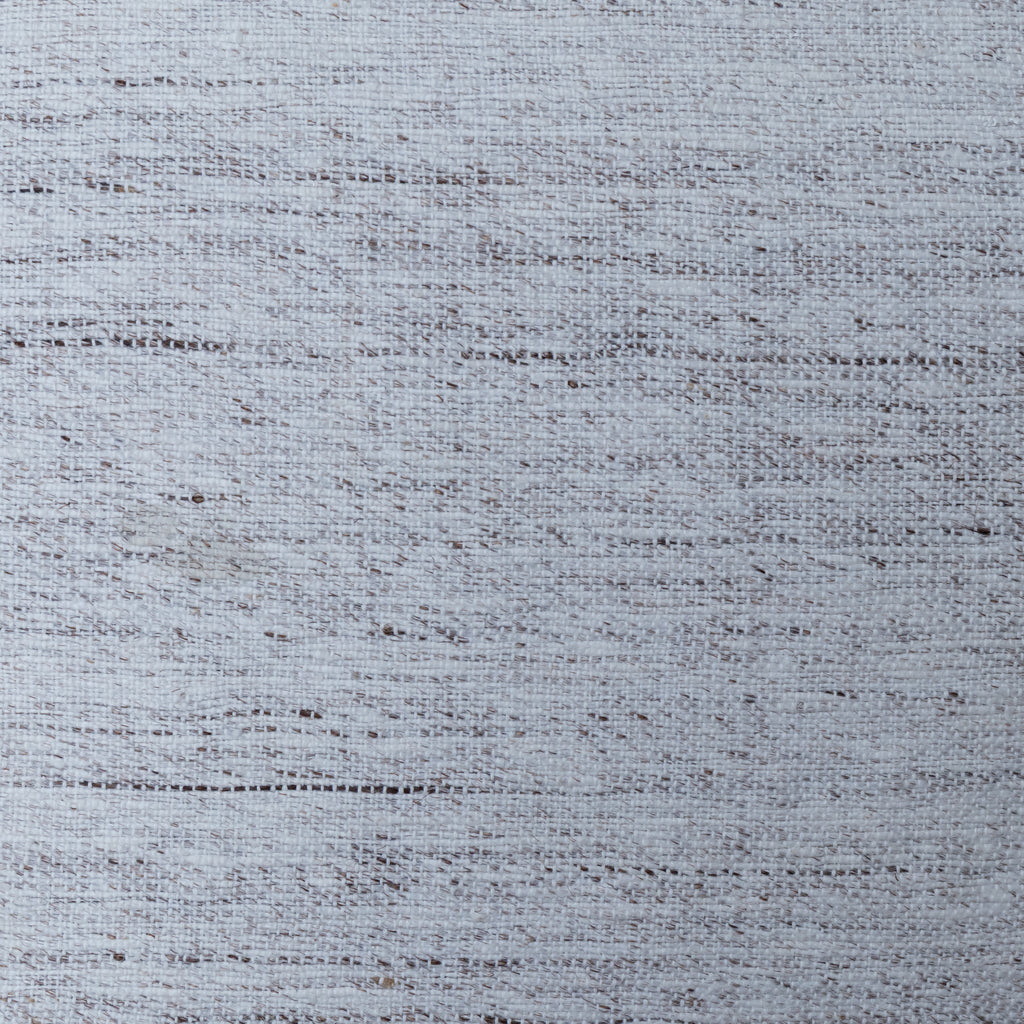 A close-up of a woven fabric texture in a light blue-gray color with subtle darker gray and brown flecks throughout.