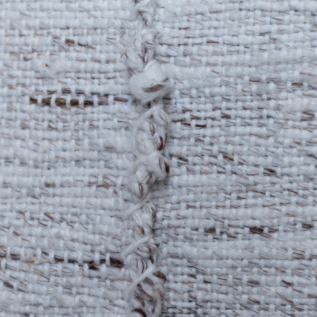 Close-up of a white woven textile with a vertical braided seam showing brown and white yarns.