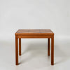 A mid-century modern wooden table with a geometric patterned top and straight legs, photographed against a neutral light gray background.