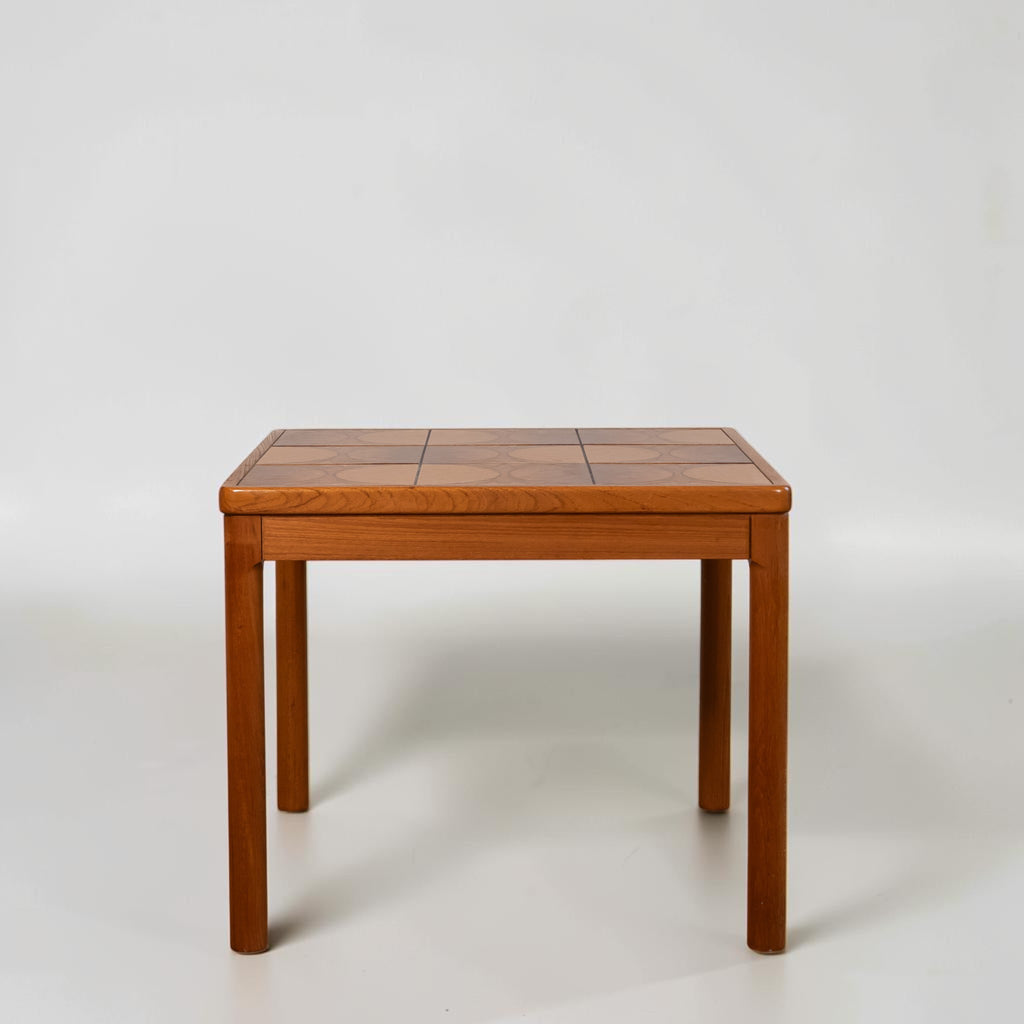 A mid-century modern wooden table with a geometric patterned top and straight legs, photographed against a neutral light gray background.