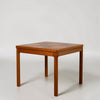 A mid-century modern wooden side table with a geometric inlaid top and four tapered legs, photographed on a seamless light gray studio background.
