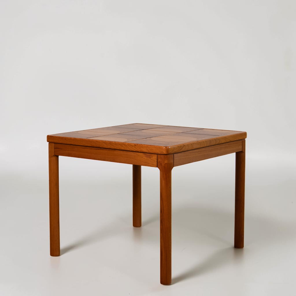 A mid-century modern wooden side table with a geometric inlaid top and four tapered legs, photographed on a seamless light gray studio background.