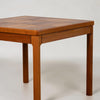 A close-up of a mid-century modern wooden table with a geometric patterned top and straight legs, shown against a neutral light gray background.