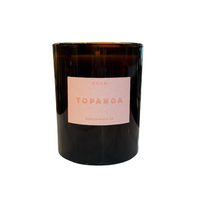 An amber glass jar candle with a pink textured label reading 'ROEN TOPANGA' on a white background.
