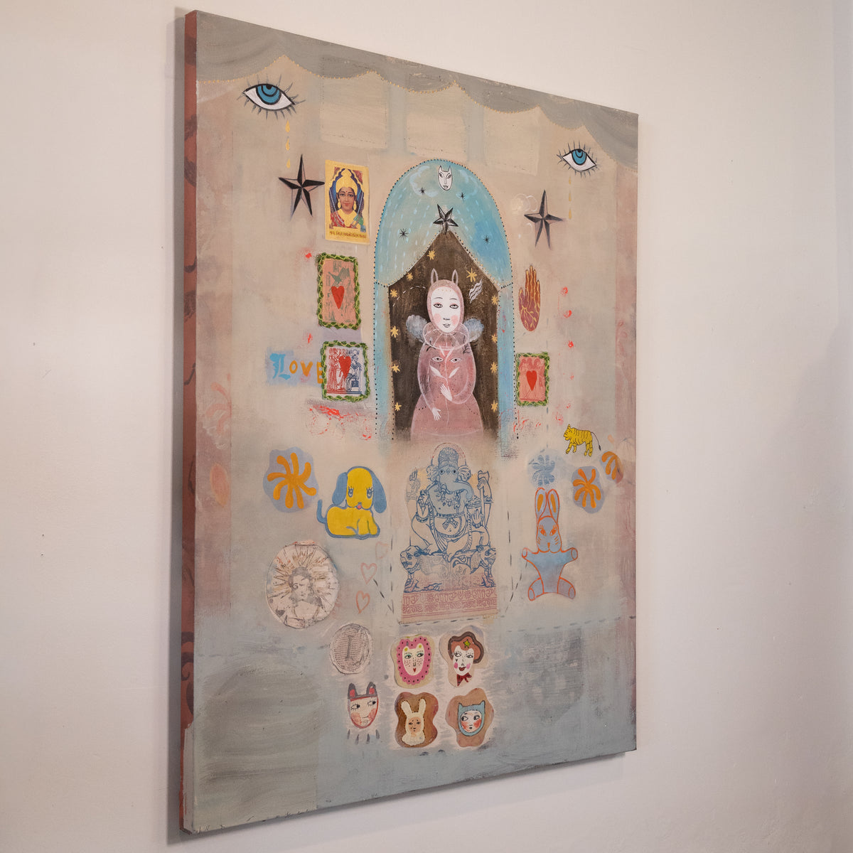 A vertical mixed-media collage painting on canvas, featuring a whimsical central figure in a pink dress under a blue arch, surrounded by stars, animal motifs, and small decorative elements on a textured beige and blue background, hanging on a white wall.