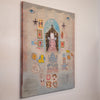 A vertical mixed-media collage painting on canvas, featuring a whimsical central figure in a pink dress under a blue arch, surrounded by stars, animal motifs, and small decorative elements on a textured beige and blue background, hanging on a white wall.