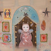 A surreal folk-art style painting featuring a central figure in a pink robe and bunny hat under a blue arch, surrounded by stars, small portraits, a heart motif, and abstract decorative elements on a beige background.