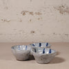 Three connected ceramic bowls with blue accents on a textured surface and background