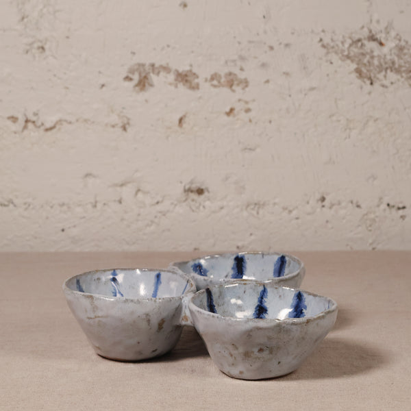 Three connected ceramic bowls with blue accents on a textured surface and background