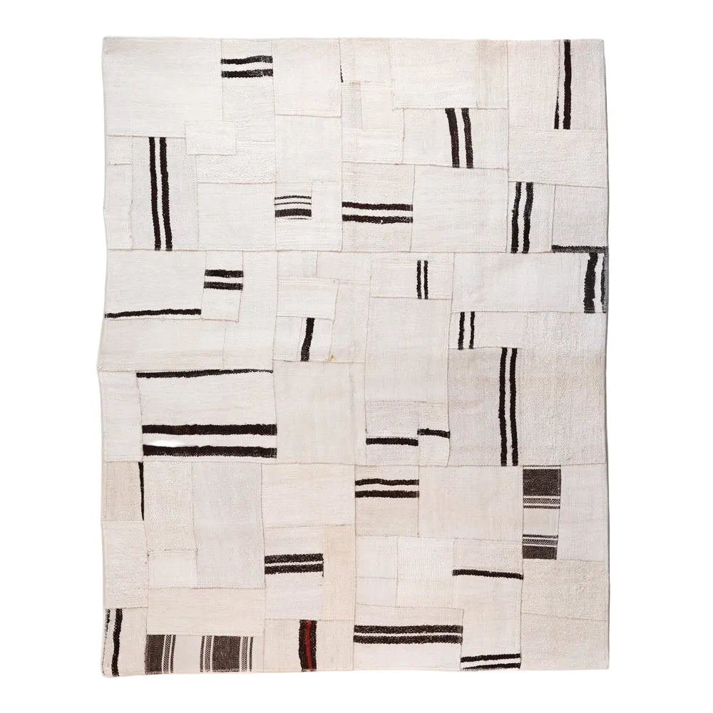 A rectangular woven rug with an abstract geometric pattern of cream, beige, and off-white squares and rectangles, accented by vertical and horizontal black stripes, shown against a plain white background.