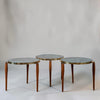 Three nesting round side tables with light blue-gray stone tops and brass rims, supported by slender brown wooden legs, photographed against a neutral light gray background.
