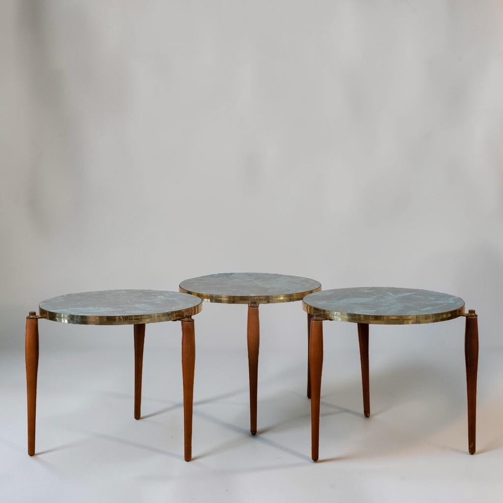 Three nesting round side tables with light blue-gray stone tops and brass rims, supported by slender brown wooden legs, photographed against a neutral light gray background.