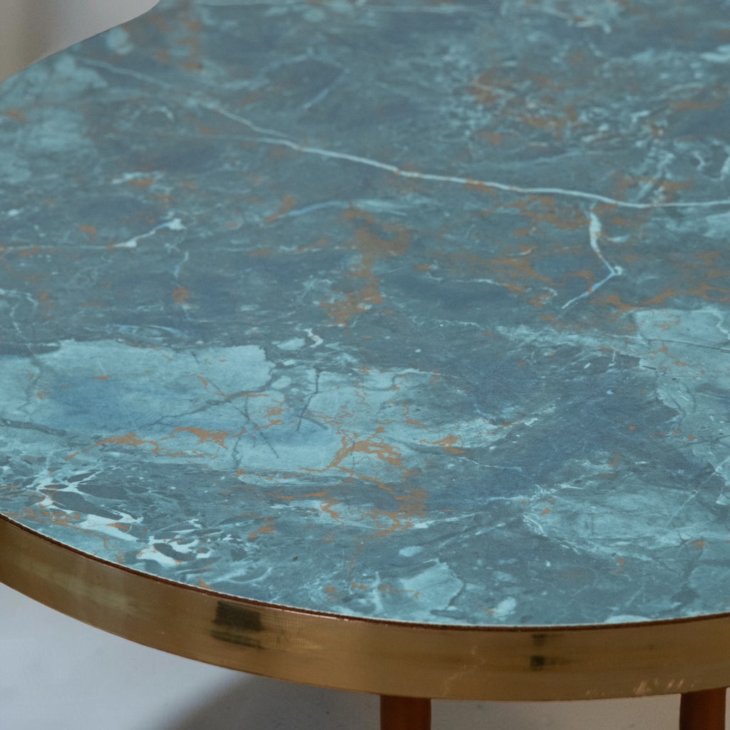 A close-up of a round table featuring a blue-green marble top with gold veining and a polished brass-colored metal rim.