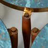 Close-up of a round side table with a distressed turquoise blue marble top, polished bronze metal apron and leg caps, and turned wood legs.