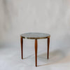 A round side table with a gray stone top, a brass rim, and three tapered brown wooden legs, photographed against a neutral light gray background.