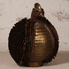 A decorative bird sculpture made from layered metallic materials, featuring a bronze-toned scaled body and dark brown feather-textured wings and neck, set against a light textured wall.