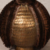 Close-up of a metallic bronze sculpture with a central rounded, scale-like textured section surrounded by layered, fringed, leaf-like extensions on a light neutral background.