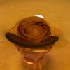 A close-up of a translucent amber glass bowl or dish with a scalloped rim, photographed against a matching warm golden background.