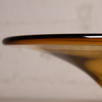 Close-up of a translucent amber glass bowl or vase rim with a glossy finish, photographed against a soft warm beige background.