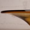 Close-up of a translucent amber glass bowl or vase rim with a glossy finish, photographed against a soft warm beige background.
