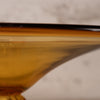 Close-up of a translucent amber glass bowl or cup with a curved rim, showing warm golden-brown tones against a soft light gray background.