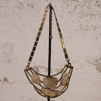 A vintage-style statement necklace with a gold-toned metal frame and five textured, organic-shaped clear resin or glass pendants, hanging on a black display stand against a textured beige wall.