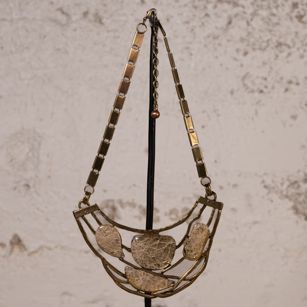 A vintage-style statement necklace with a gold-toned metal frame and five textured, organic-shaped clear resin or glass pendants, hanging on a black display stand against a textured beige wall.
