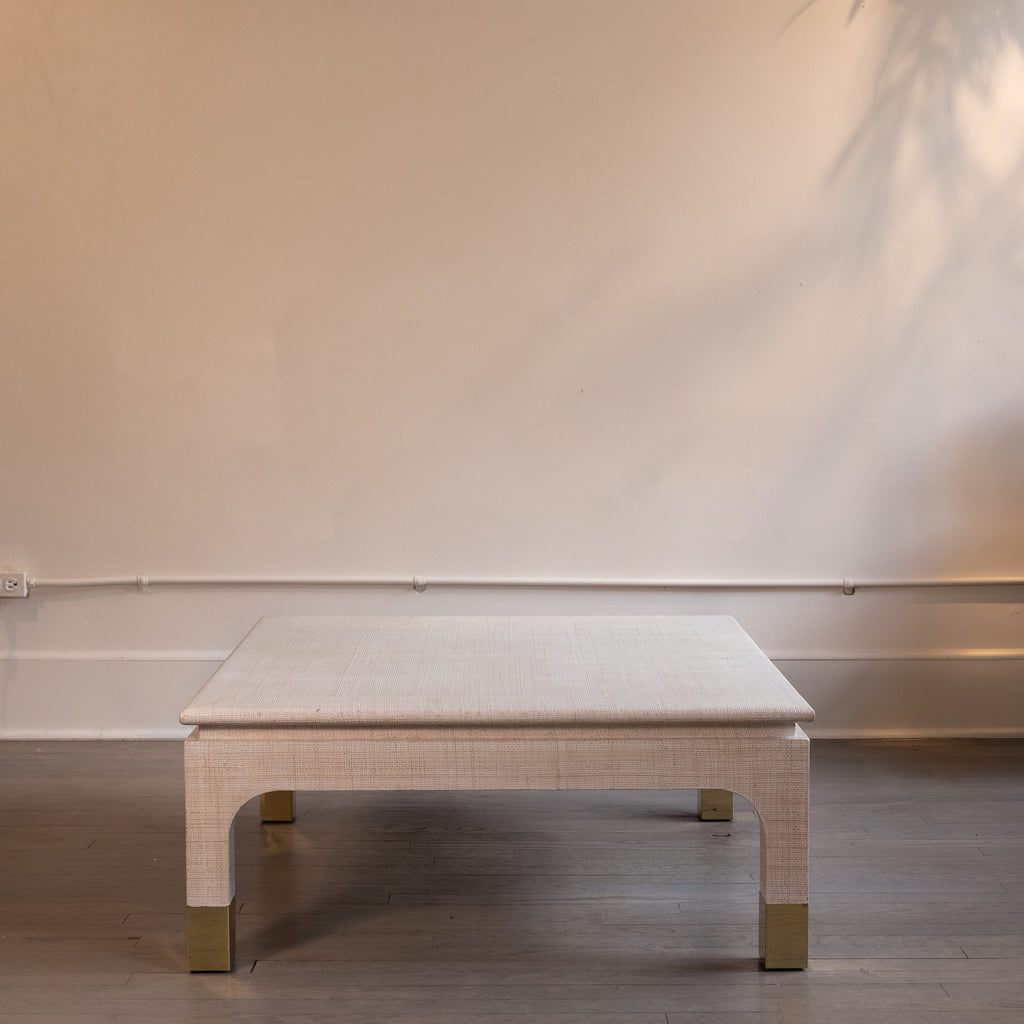 Square table with a textured surface and gold legs against a plain wall.