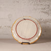 Decorative ceramic plate with a scalloped edge on a stand against a textured wall.