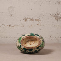 Small ceramic pot with green and blue patterns on a textured surface