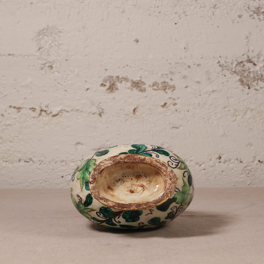 Small ceramic pot with green and blue patterns on a textured surface