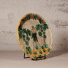 A vintage hand-painted ceramic plate displayed on a small black metal stand against a textured, light beige plaster wall.