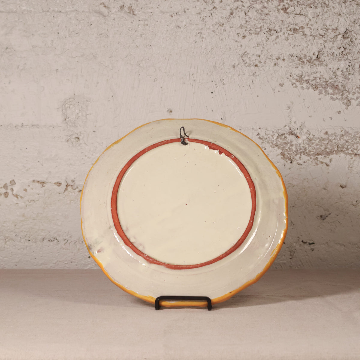 Round ceramic plate with a red rim on a stand against a textured wall.