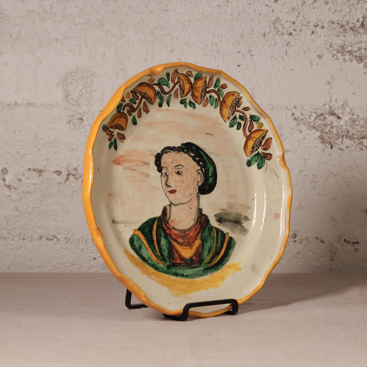 Decorative plate with a painted portrait on a stand against a textured wall.