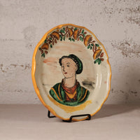 Decorative plate with a painted portrait on a stand against a textured wall.