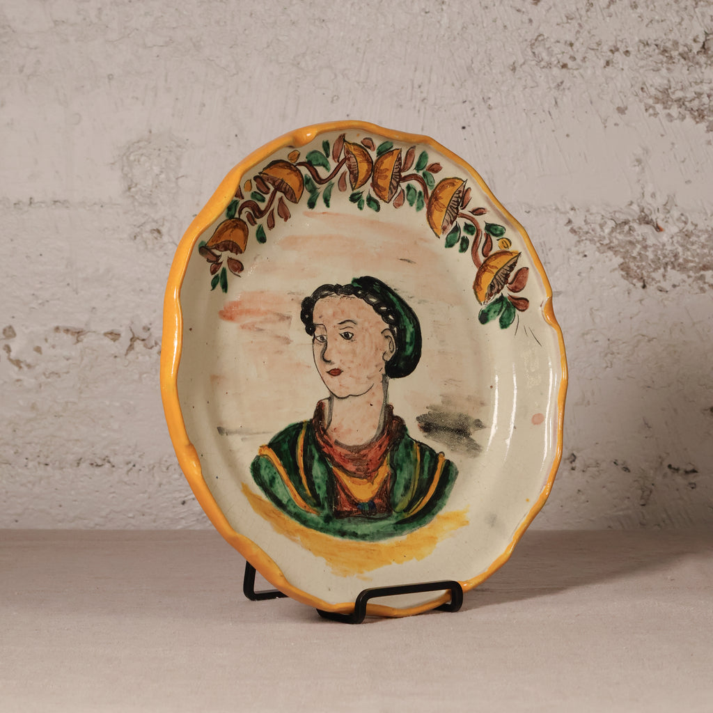Decorative plate with a painted portrait on a stand against a textured wall.