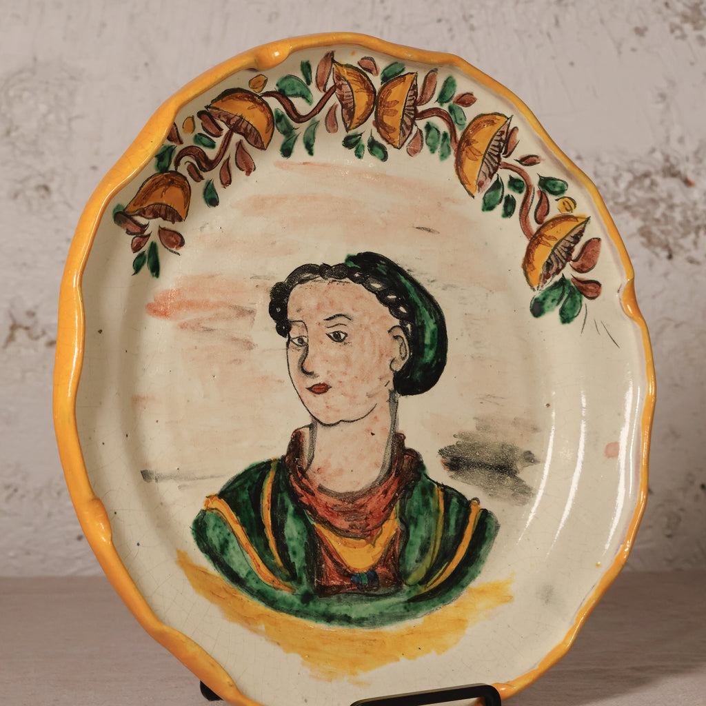 Ceramic plate with a painted portrait of a woman and decorative elements on a textured wall background