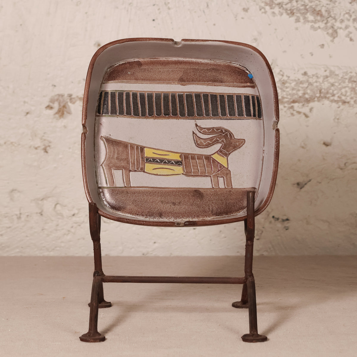 A vintage-style metal desk fan with a brown enamel finish and an Egyptian cartouche design featuring a baboon on the front, supported by four metal legs.