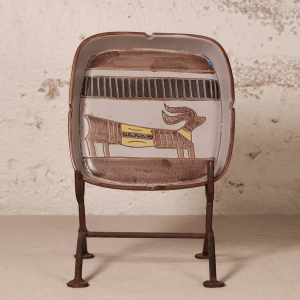 A vintage-style metal desk fan with a brown enamel finish and an Egyptian cartouche design featuring a baboon on the front, supported by four metal legs.