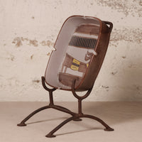 A decorative ceramic ashtray featuring a vintage car illustration, displayed on a rusted metal stand against a textured, distressed off-white wall.