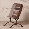 A decorative ceramic ashtray featuring a vintage car illustration, displayed on a rusted metal stand against a textured, distressed off-white wall.