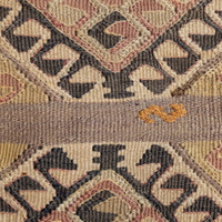 Close-up of a woven textile with a geometric pattern in beige, brown, muted pink, and charcoal, plus a horizontal band with a small orange motif.